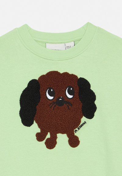 Sweatshirt verde com um desenho de um cão castanho em estilo cartoon, com olhos grandes e orelhas pretas, bordado na área do colar.