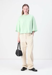 Svijetlozeleni kratki majica, širokog kroja, uparen s bež hlačama širokih nogavica. Crna torba i cipele dodaju kontrast odjevnoj kombinaciji.