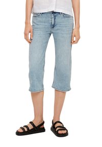 Jasnoniebieskie dżinsowe spodnie capri o luźnym kroju, z podwiniętym dołem i pięcioma kieszeniami, zestawione z czarnymi sandałami na paski.