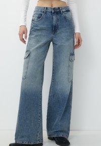 Ljust blå denim cargobyxor med hög midja, vida ben, två sidofickor och en bleknad färggradient. En klassisk femfickorsdesign.