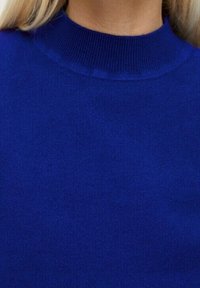 Pull bleu roi, texture côtelée, col montant haut, tissu doux. Design simple, sans motifs ni détails supplémentaires visibles.