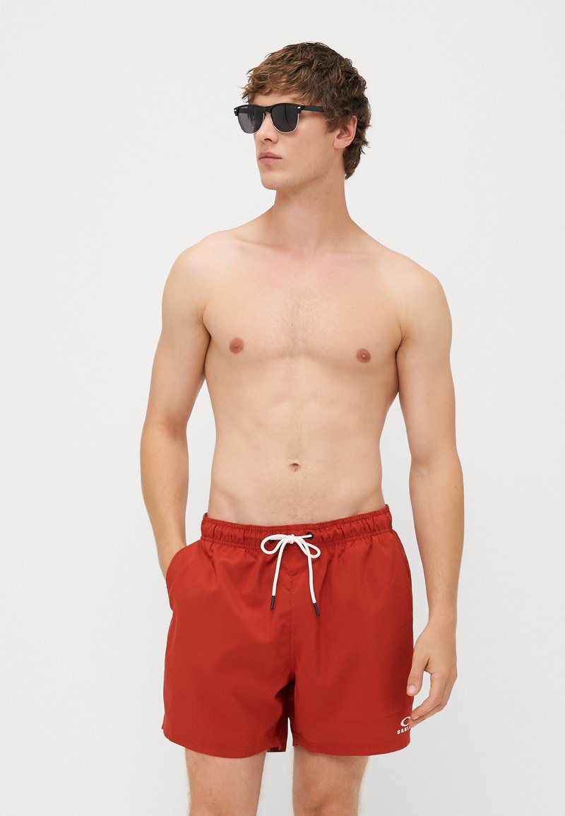 COSTUMI DA BAGNO ROSSI CON CORDINO, VITA ELASTICA, TASCA LATERALI E LOGO SULL'ORLO INFERIORE. CORTI E CON UNA TEXTURA LISCIA.