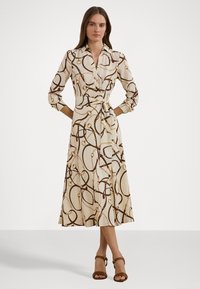 Beige wrap dress with a chain pattern, featuring a collared neckline, long sleeves, waist tie, and a flared hem. Worn with brown strappy heels.