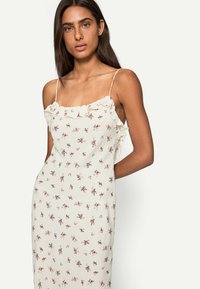 Abito slip floreale in crema chiaro con scollatura arricciata e spalline sottili. Presenta un motivo floreale sparso in tonalità di rosa e verde.