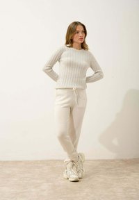 Pull en maille côtelée gris clair à manches longues, associé à un pantalon jogger assorti en tissu doux avec cordon de serrage ajustable. Porté avec des baskets.