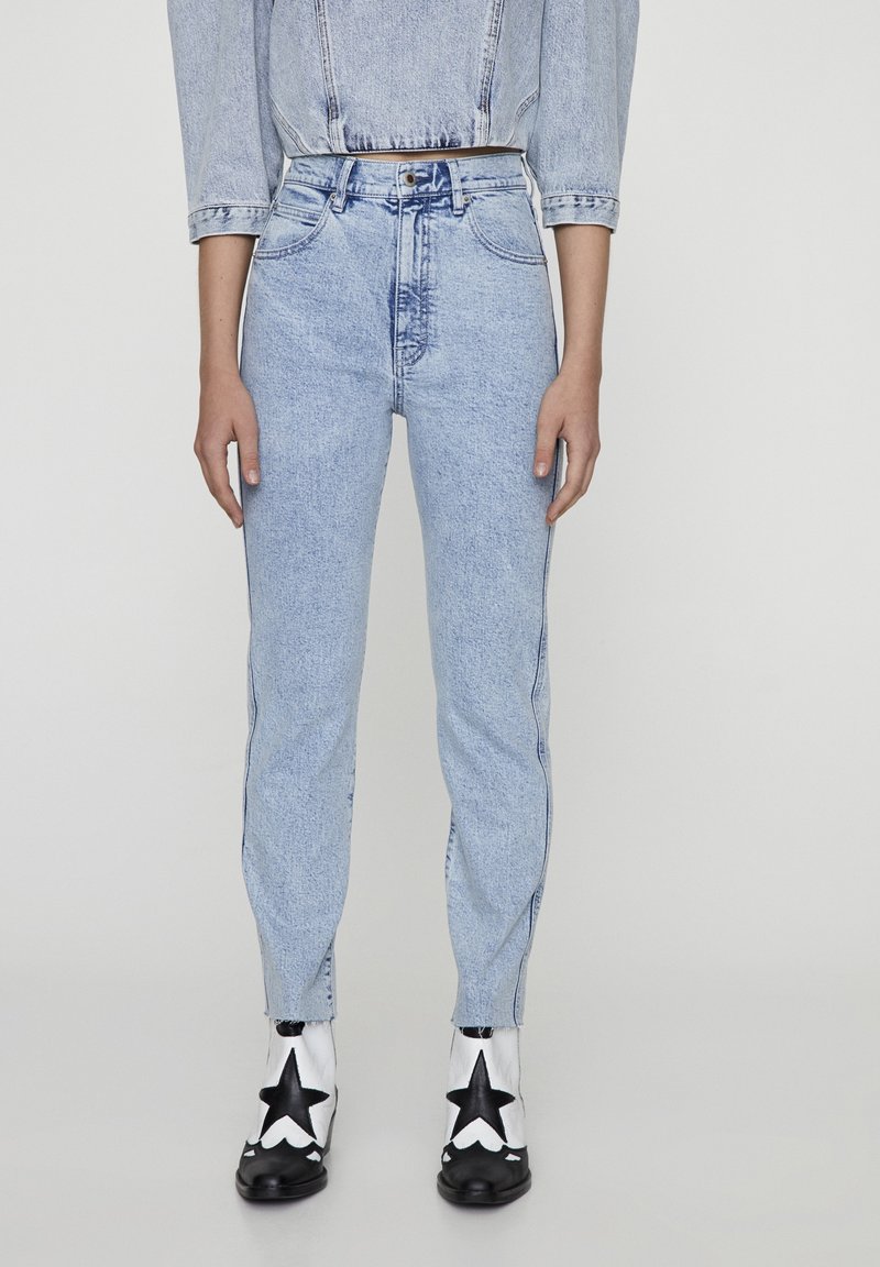 Jean taille haute bleu clair porté avec une veste en jean courte et des bottines blanches avec de grandes étoiles noires à l'avant.
