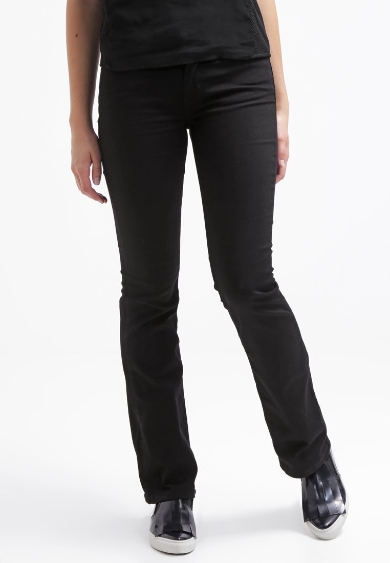 Svarta denimjeans med en figurnära silhuett, som har en slät textur och en traditionell fem-fickorsdesign. Bärs med svarta sneakers.