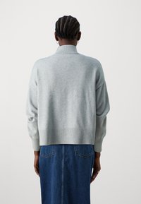 Ljusgrå, kortärmad tröja med ribbad krage och ärmslut, kombinerad med en blå denimkjol med två bakfickor. Slät textur och avslappnad passform.