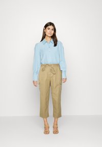 Camisa de botão azul-claro com mangas longas, combinada com calças cargo bege com um laço ajustável na cintura e bolsos. Sandálias completam o visual.