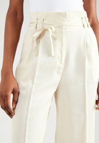 Crème-kleurige hoge taille broek met wijde pijpen, voorzien van een gestructureerde afwerking, riemlussen en een stoffen riem die rond de taille is geknoopt.