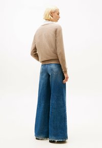 Brązowy sweter z okrągłym dekoltem, zestawiony z dżinsami o szerokich nogawkach w niebieskim kolorze z postrzępionym dołem i klasycznymi tylnymi kieszeniami.