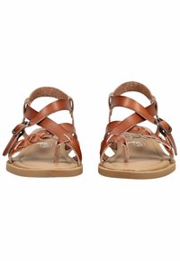 Hnědé kožené sandály s pletenými a překříženými pásky, nastavitelnou sponou a plochými béžovými podrážkami zobrazené zepředu.