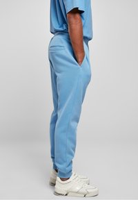 Ljusblåa träningsbyxor med sidofickor, smalnande design och elastiska muddar, tillsammans med vita sneakers som har en synlig luftdämpning.