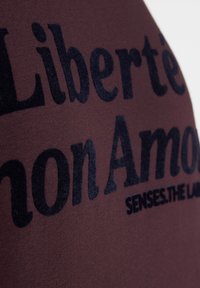 Maroon cotton fabric featuring large black print text. The text includes "Liberté" and "SENSES.THE LAND," with a soft, smooth texture.
