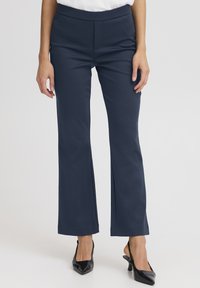 Tengerészkék szabott nadrág egyenes szárú kialakítással, lapos derékpánttal és sima textúrával. Feketére hegyezett magassarkú cipővel párosítva.