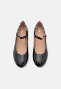 Chaussures en cuir verni noir avec bout rond et bride à boucle sur le côté. Texture lisse et doublure intérieure beige. Design simple.