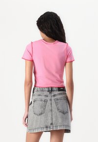 Ροζ κοντομάνικη μπλούζα, με ακατέργαστα τελειώματα. Συνδυάζεται με μια ψηλόμεση, ξεθωριασμένη γκρι τζιν φούστα, με δύο πίσω τσέπες.