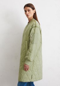 Gevoerde groene lange jas met een ritssluiting aan de voorkant, ribgebreide manchetten en een zijzak, met een getextureerd golvend patroon.