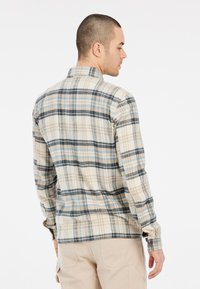 Geklede blouse van zacht stof in beige, blauw en zwart. Kenmerken zijn een kraag, lange mouwen en knoopmanchetten met een gebogen zoom.