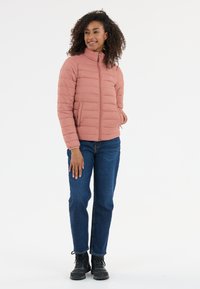 Lyserød pufferjakke med ståkrave og lynlås fortil, med vandret syninger og to sidelommer, parret med blå jeans og sorte støvler.