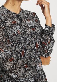 Haalit kukkakuosiset, läpikuultavat mustat blouset, joissa on kermaa ja punaista; siinä on pyöreä pääntie, nappikiinnitys ja rypytetyt hihat.