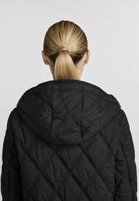 Czarna pikowana kurtka z kapturem, z diamentowym wzorem i gładką teksturą. Widok z tyłu pokazuje włosy w niskim kucyku.