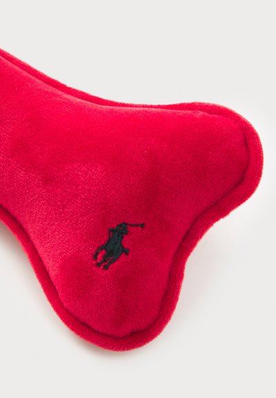 Rød plyshundelek i benform med en svart brodert logo. Myk, teksturert overflate med sydd kanter for holdbarhet.