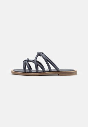 Sort flad sandal med flere knudede stropper og en tynd træsål på en ensartet lys baggrund.