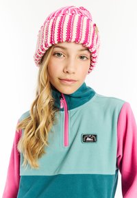Gehaakte beanie met roze en witte strepen, gecombineerd met een teal en roze fleece trui met een ritskraag en een merklogo patch.
