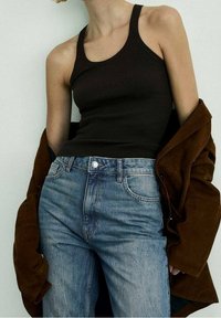 Canottiera a coste marrone indossata con jeans in denim azzurro chiaro e una giacca esterna marrone, caratterizzata da una vestibilità comoda e una vita visibile.