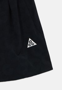 Peça de vestuário em tecido preto com um logótipo triangular branco com a inscrição "acg", textura suave e design plissado em estilo casual.