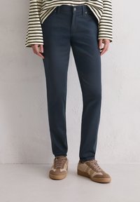 Marin blauwe chino's van gladde stof, met een klassieke pasvorm, zijzakken en gecombineerd met lichtbruin gestructureerde sneakers.