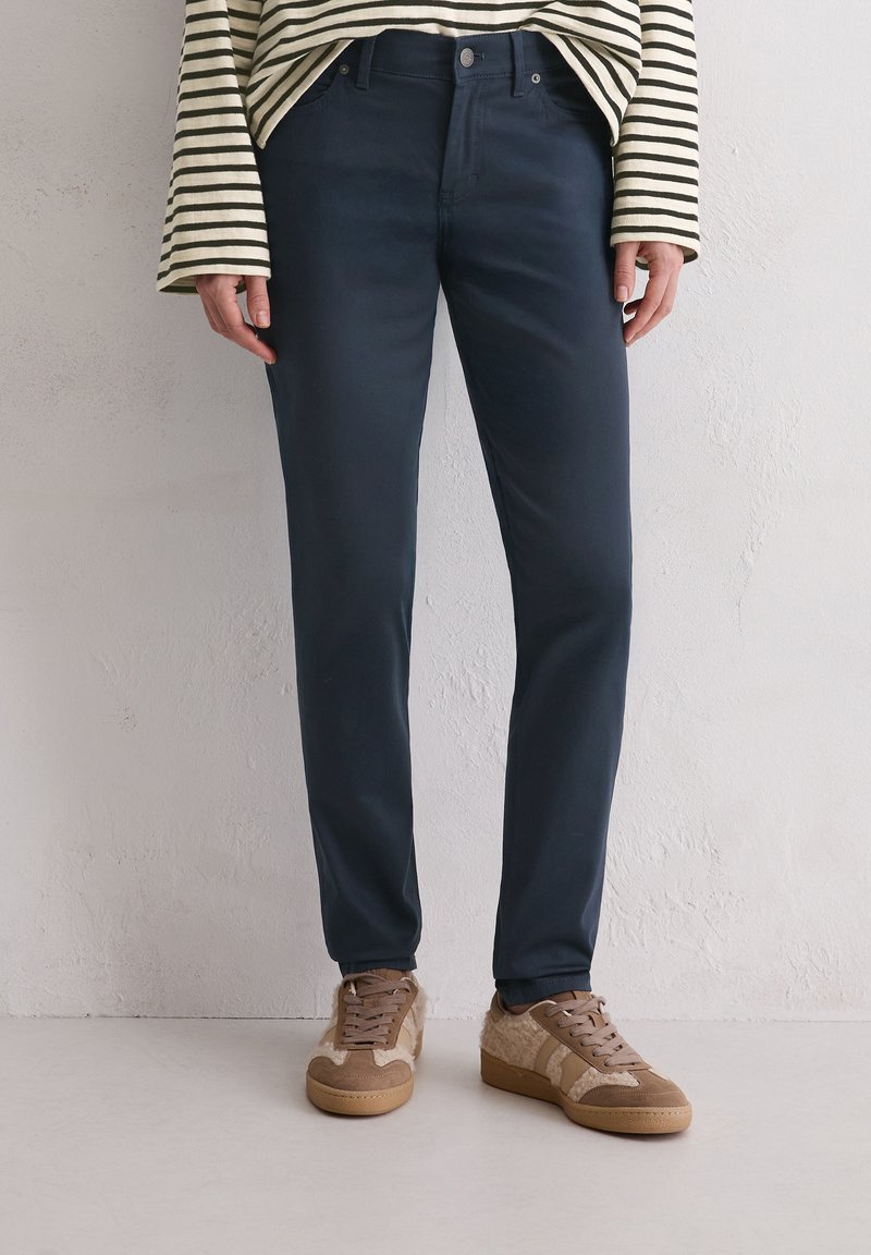 Marin blauwe chino's van gladde stof, met een klassieke pasvorm, zijzakken en gecombineerd met lichtbruin gestructureerde sneakers.