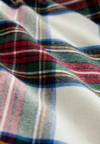Țesătură din lână cu un model tartan, având linii verzi, roșii, albastre și galbene pe un fundal crem, texturată și moale.