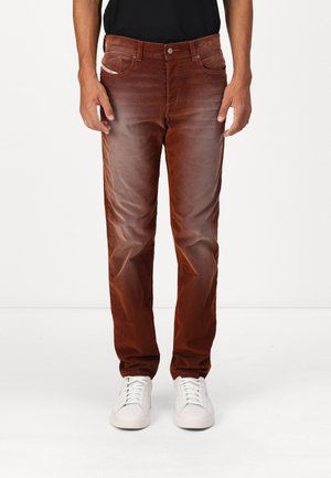 Brune denim-bukser med en falmet finish, lige ben-design, fem-lomme styling og metalknotter, båret med hvide sneakers.