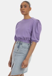 Lilla cropped sweatshirt med pufærmer og elastisk talje, parret med en lys blå denimnederdel med en frontslids og frynset kant.