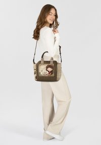 Braune und beige Handtasche mit einer strukturierten Oberfläche, versehen mit einer verspielten Mädchenillustration, doppelten Griffen und einem abnehmbaren Schulterriemen.