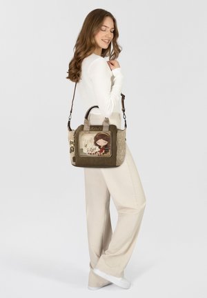 Braune und beige Handtasche mit einer strukturierten Oberfläche, versehen mit einer verspielten Mädchenillustration, doppelten Griffen und einem abnehmbaren Schulterriemen.