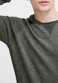 Olijfgroen sweatshirt met lange mouwen, voorzien van een gemêleerde textuur, ribbelboord aan de hals en een V-stiksel detail op de kraag. Zacht en casual fit.