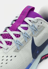 Παπούτσι για trail running της Nike σε ανοιχτό γκρι με ροζ και μπλε λεπτομέρειες, με υφασμάτινο πλέγμα στο επάνω μέρος, παραδοσιακό κορδόνι και ανθεκτική σόλα.