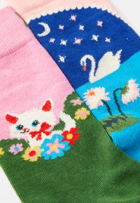 Colorful knitted socks featuring a white cat and flowers on a pink and green background; blue section with swan and moon patterns.