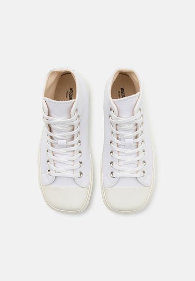 Höga sneakers i vitt kanvas med vita skosnören och silverfärgade öglor. Har en rund gummikant vid tårna och en mjuk inre klädsel.