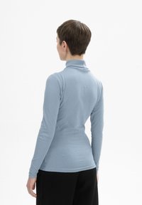 Hellblau, langärmliger Rollkragenpullover mit taillierter Passform und weicher Textur, kombiniert mit schwarzen, lockeren Hosen.