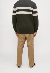 Dunkelgrüner Strickpullover mit horizontalen cremefarbenen und grauen Streifen, kombiniert mit beigen, lässig geschnittenen Cargo-Hosen und schwarzen Sneakers.