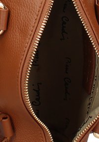 Bruine gestructureerde leren tas met een open gouden rits die een donkere binnenkant toont, gevoerd met het "Pim Cardy" logo opdruk.