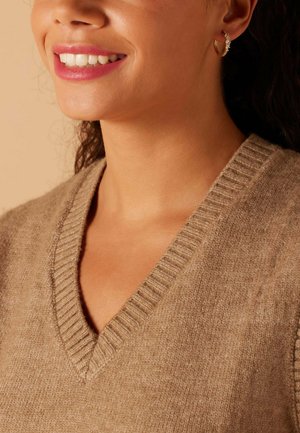 Pull brun à col en V avec une texture côtelée, en tissu doux et avec une coupe décontractée. Boucle d'oreille dorée avec des accents en cristal est visible.