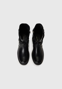 Paire de bottines en cuir noir avec bouts ronds et sangles à boucle, vue de dessus sur un fond clair uni.