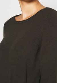 Dunkelgrüner Pullover mit Rundhalsausschnitt, weichem Strickmaterial und leicht lässiger Passform. Nahtdetails sind an den Schultern und zur Seite sichtbar.