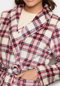 Rochie din fleece cu un model în carouri roșii, bleumarin și crem. Prezintă un guler tip șal, talie cu curea și buzunare laterale. Textură moale.