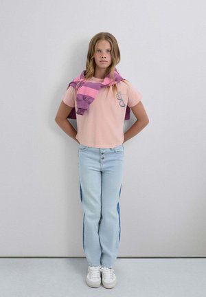 Camiseta de manga corta rosa claro con un diseño bordado, combinada con vaqueros azul claro con paneles laterales azul oscuro y zapatillas blancas.